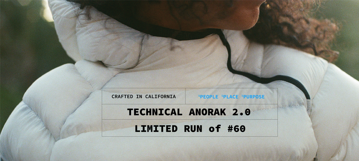A person wearing the cocoon anorak in white, seen over the shoulder, with a plate reading: Crafted in California. People, place, purpose. Technical anorak 2.0. Limited run of #60.